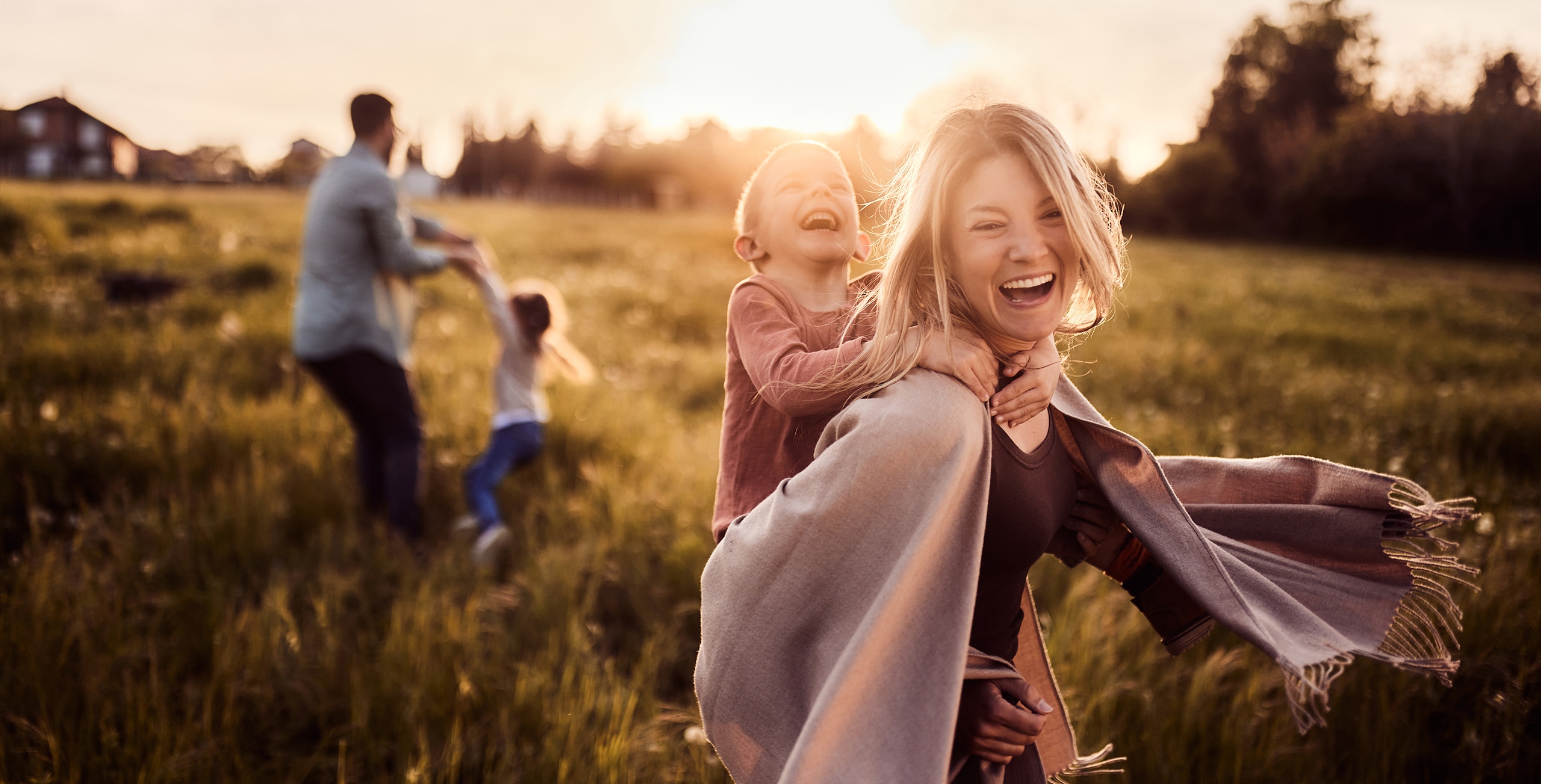 Carefree woman having fun while piggybacking her small son in the park at sunset. There are people in the background. Copy space.